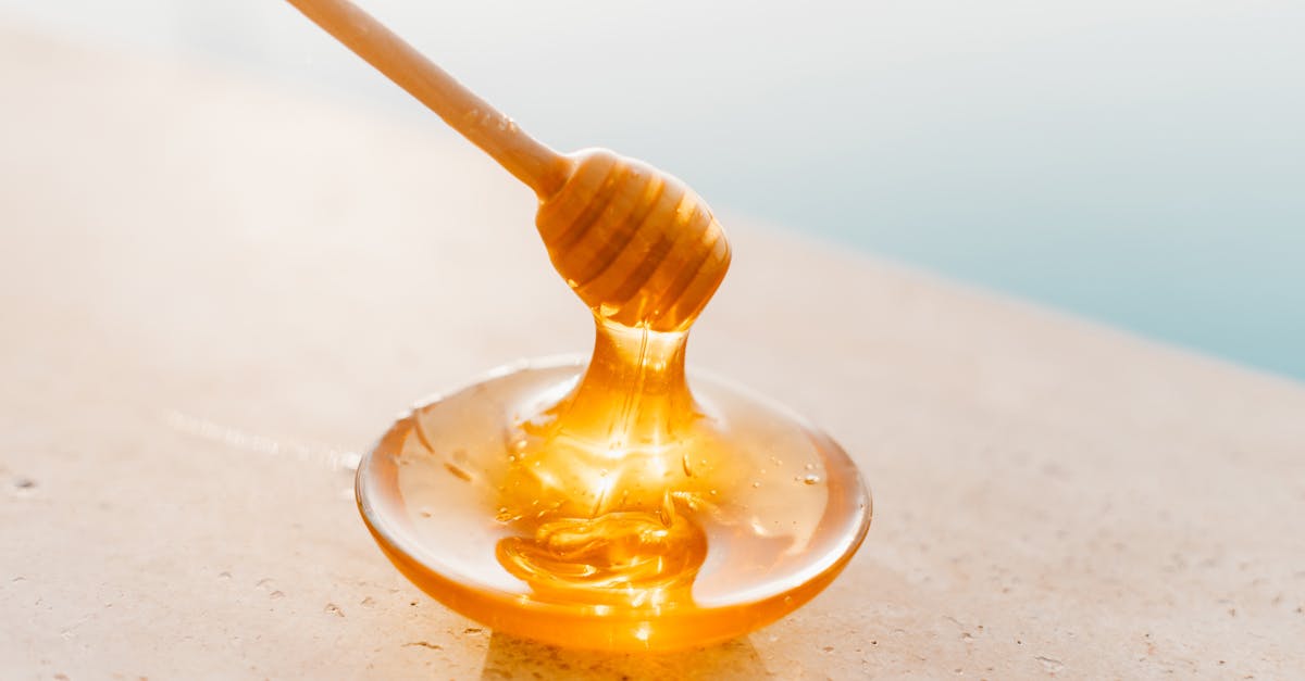 Golden honey flowing from a wooden dipper onto a glass plate, captured in warm daylight.